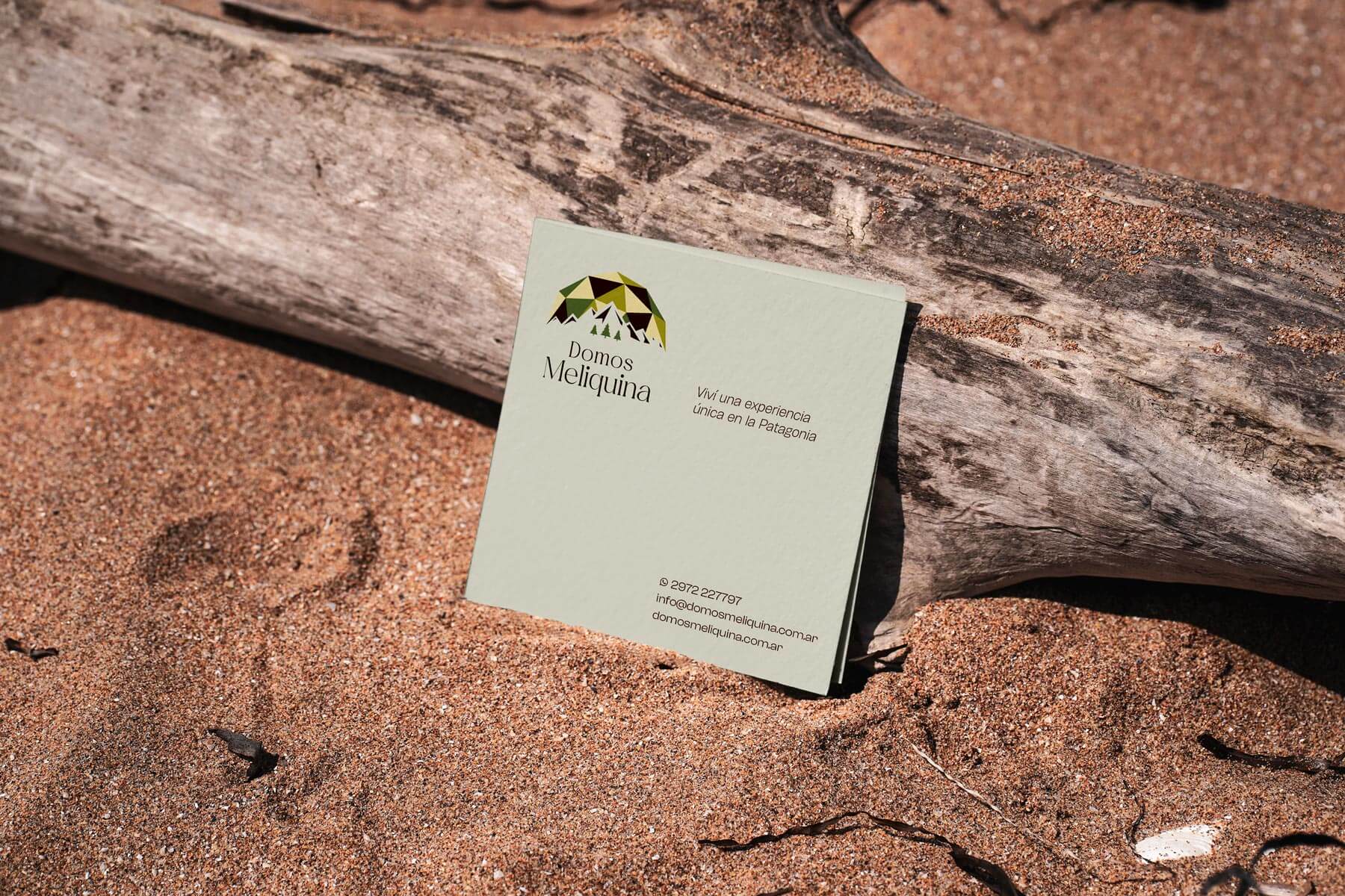 Card laying in the sand with printed Domos Meliquina logo